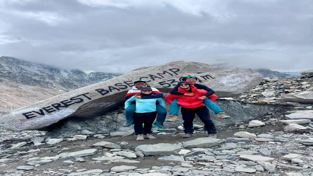 Four trekkers celebrating at Everest Base Camp 5364m marker stone with Himalayan mountains, Nepal